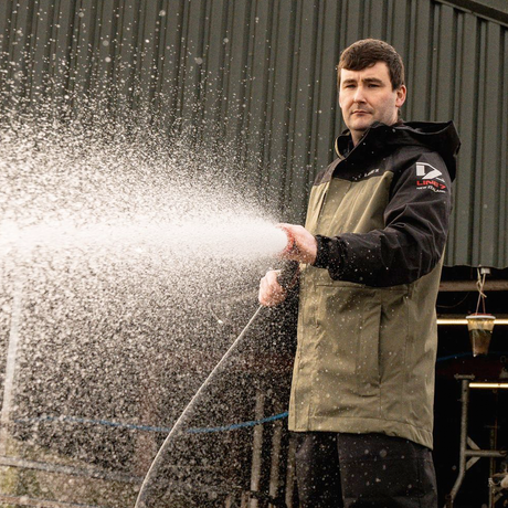 Man in a Line7 Storm Pro20 waterproof jacket holding a hose, spraying water outdoors.